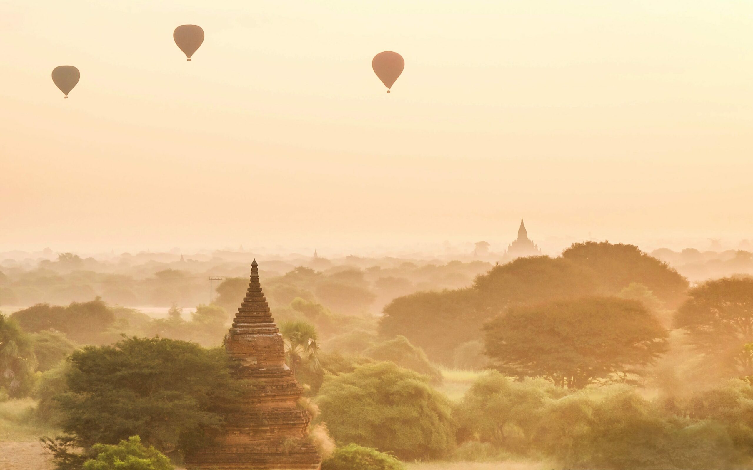 Image taken of a sunset in Myanmar that I imagine might resemble the fictional Air Temple described in "Avatar: The Last Air Bender", the image includes old building and a green forest with hot air balloons in the distance